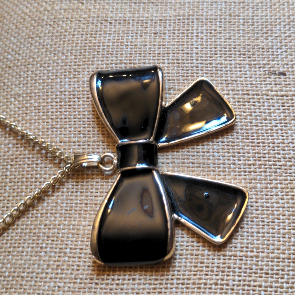 Black Enamel Bow with a long gold tone chain necklace.